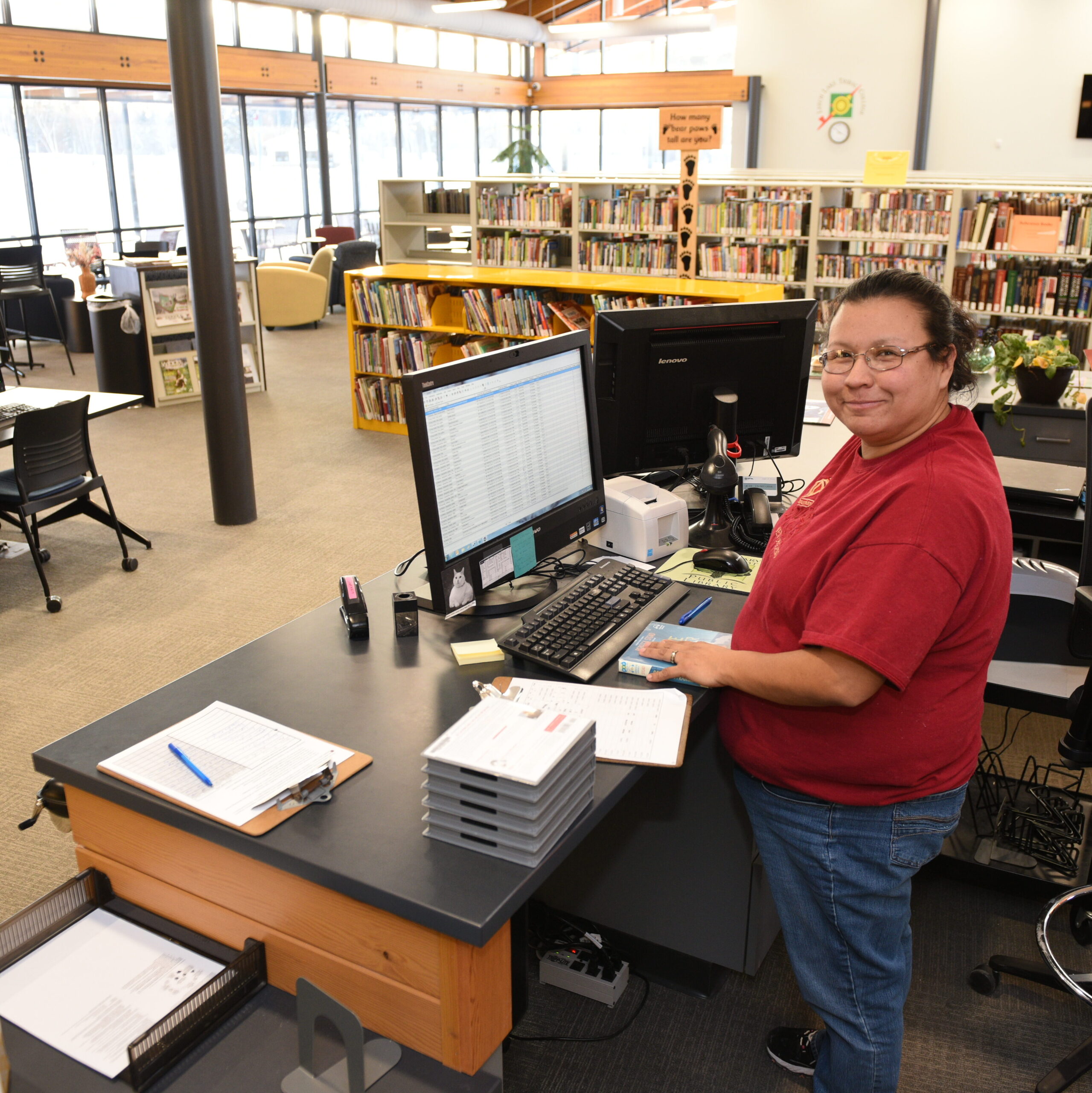 A library worker at an information desk near bookcases and computers