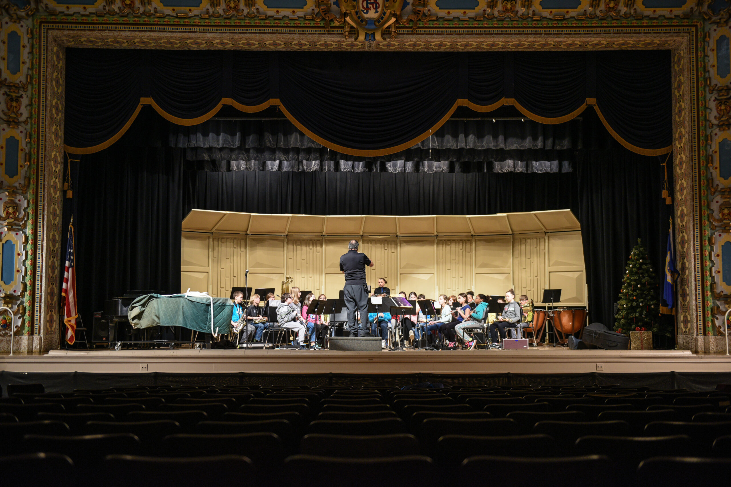 A youth orchestra on a historic stage with an adult conductor
