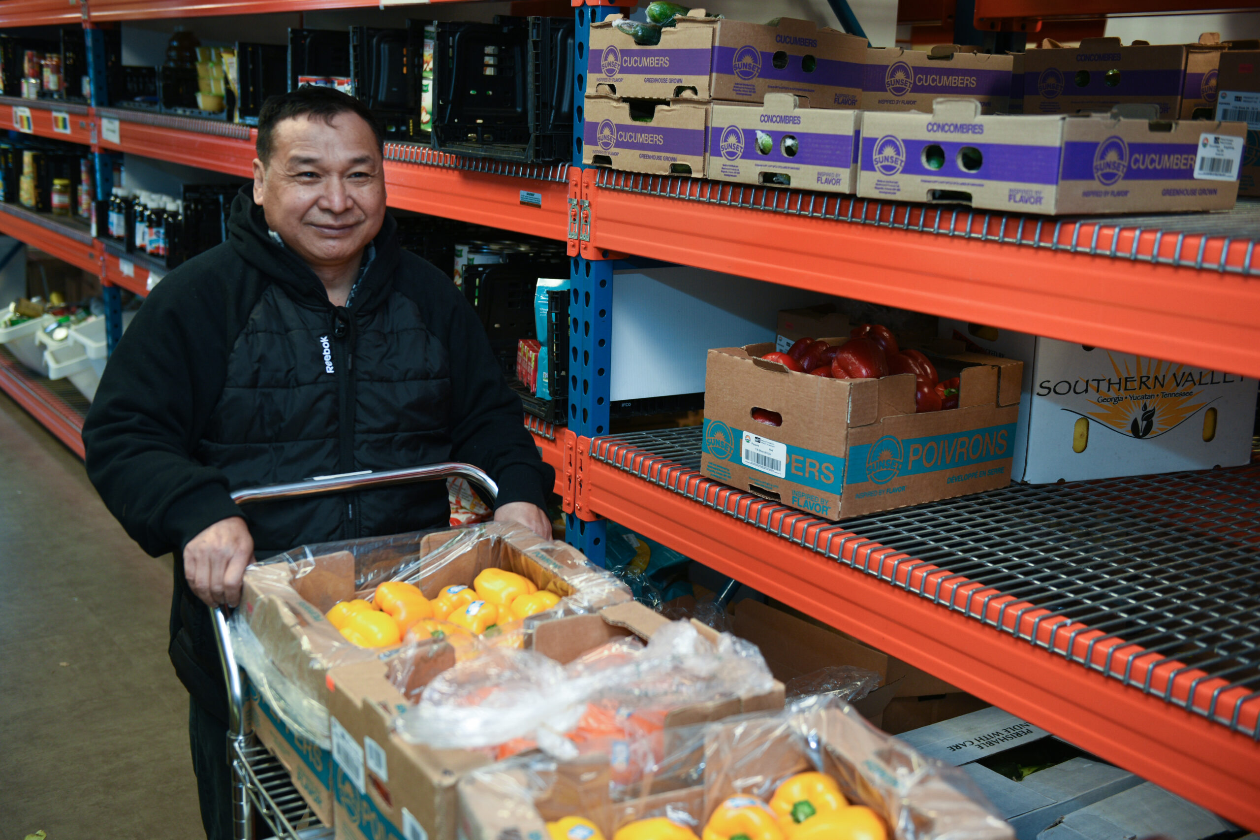 A smiling person pushing a cart of food at a food shelf distribution center