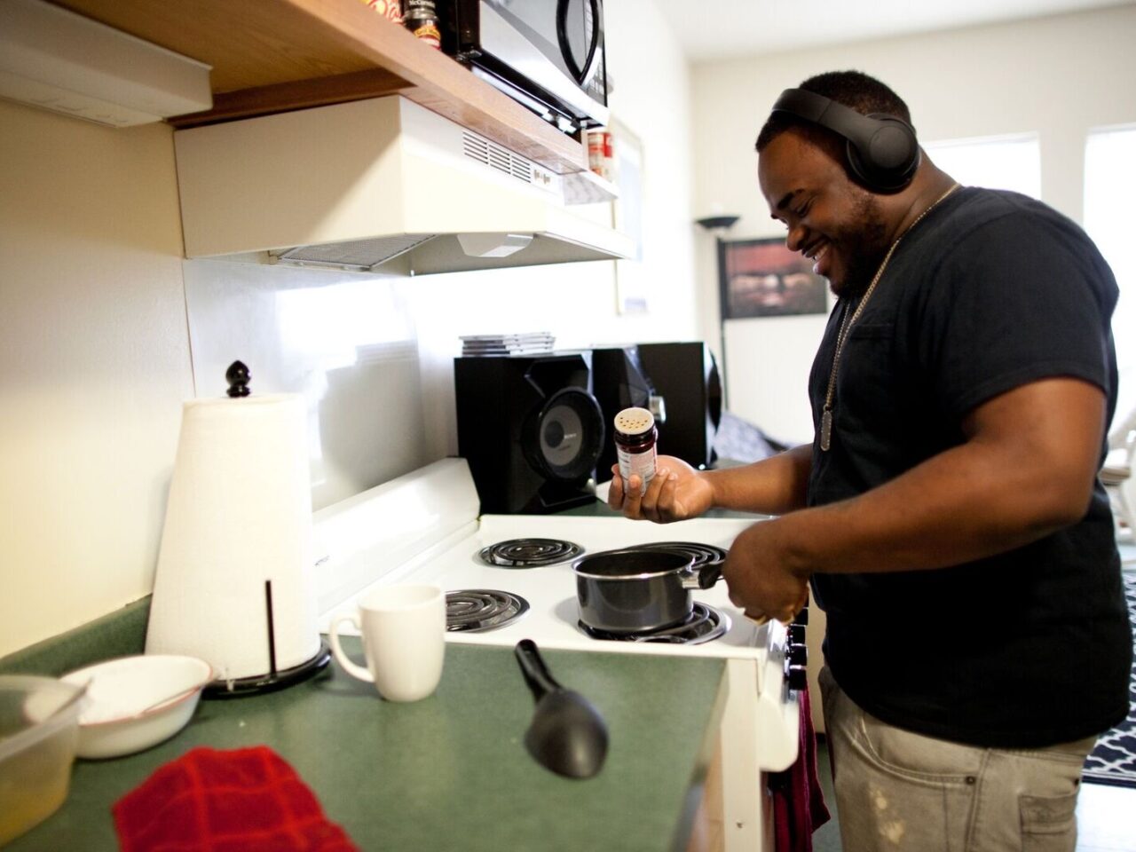 Smiling young adult wearing headphones cooking over a stove