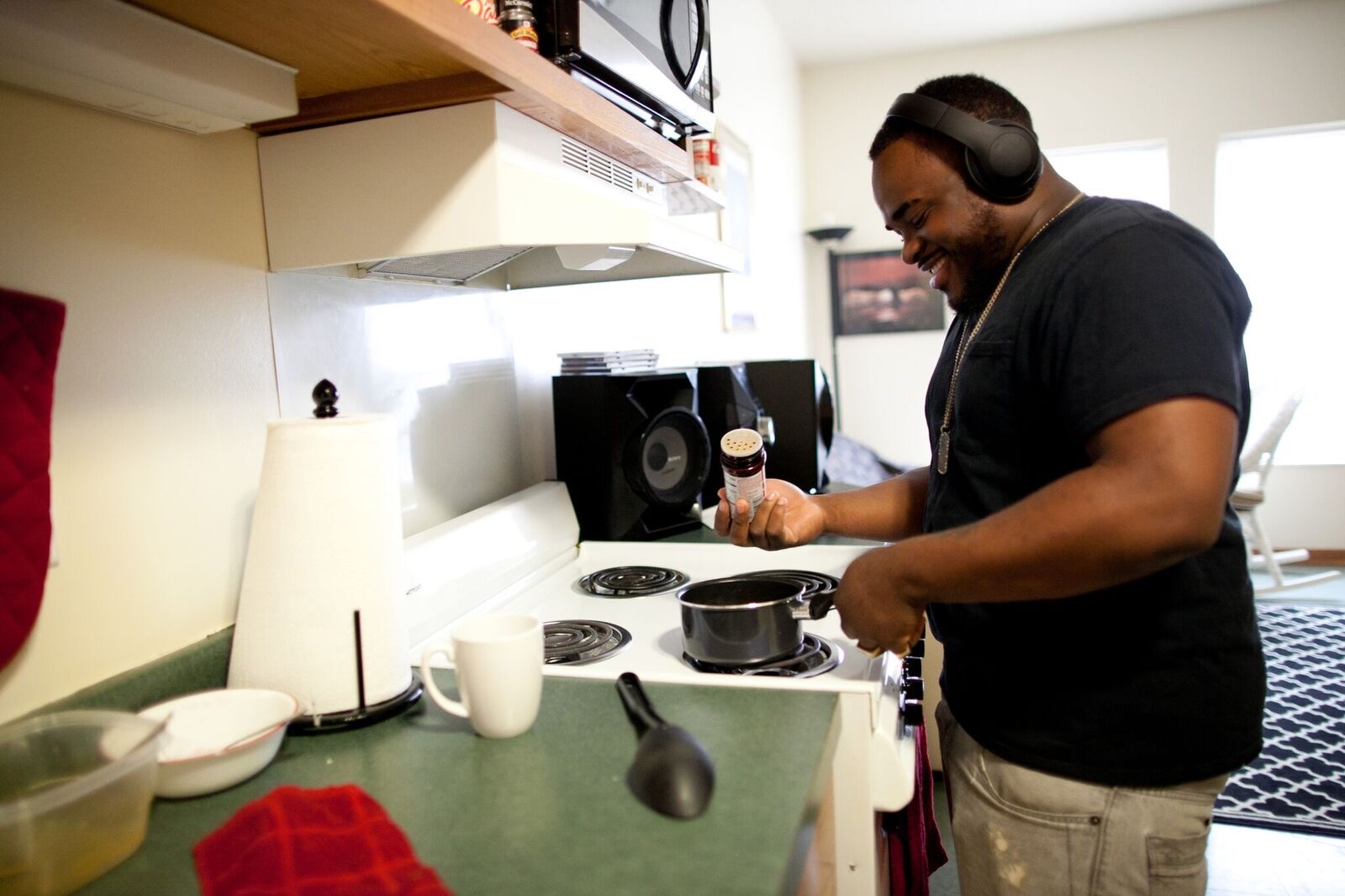 Smiling young adult wearing headphones cooking over a stove