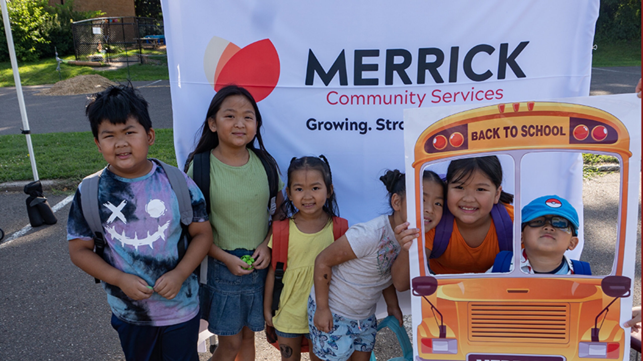 Six children posing with a school bus cutout