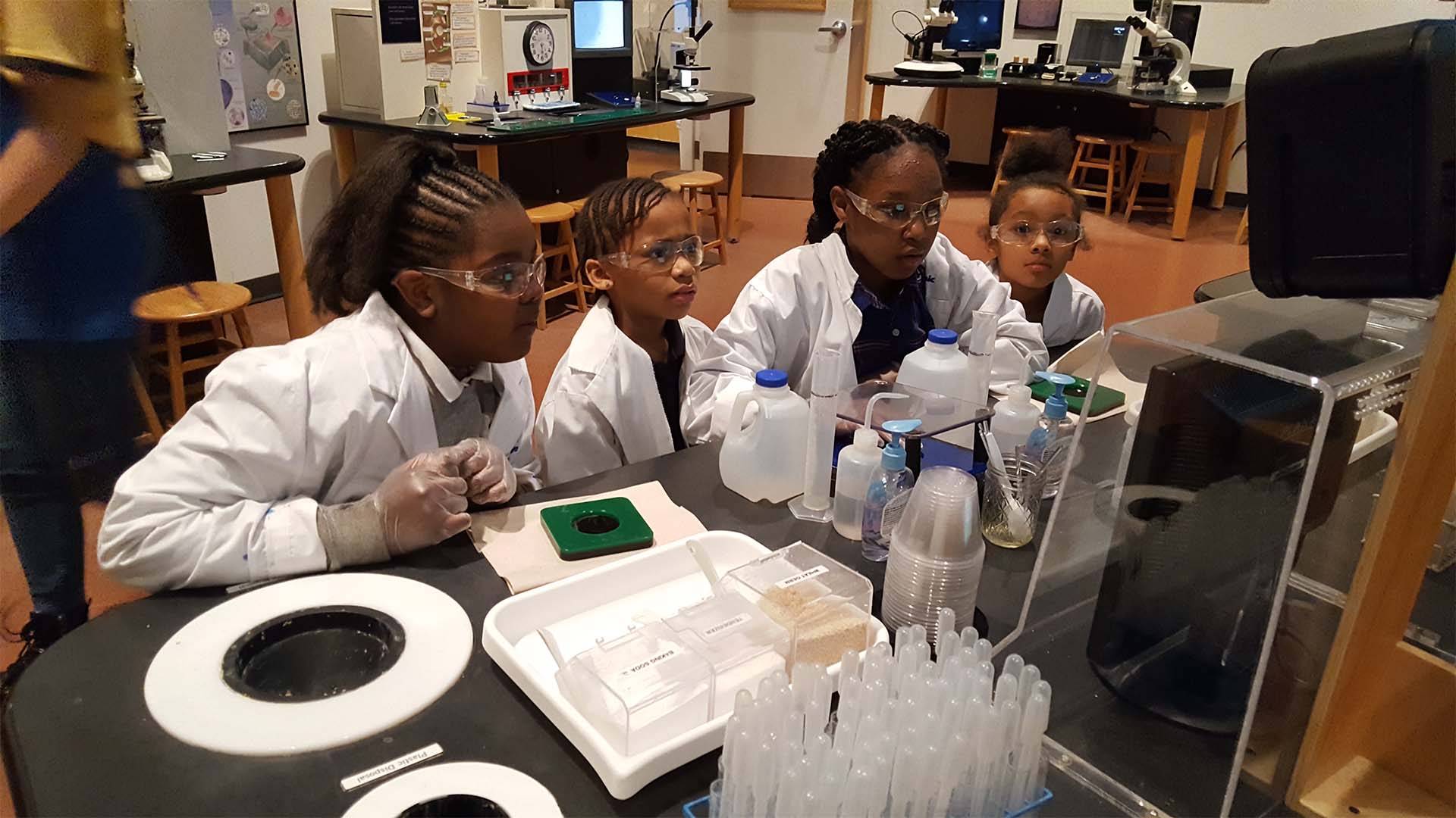 4 students in lab coats in a classroom